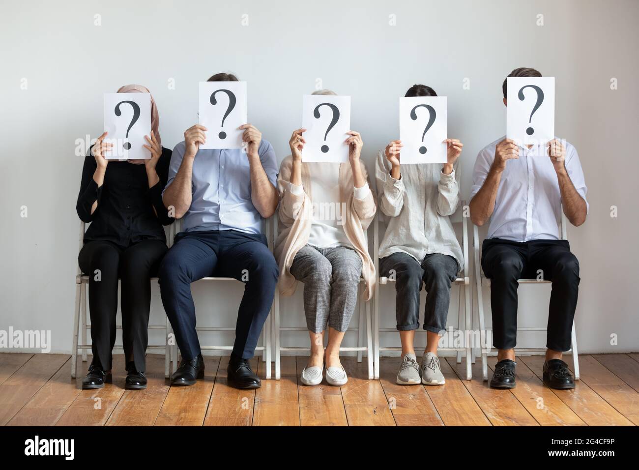 Verschiedene Jobkandidaten verbergen Gesichter hinter Blättern mit Fragezeichen Stockfoto