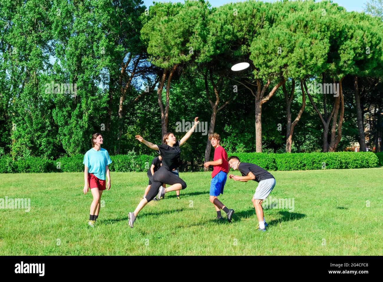 Gruppe von gemischten jungen Teenagern Menschen in Freizeitkleidung spielen mit Kunststoff fliegende Scheibe Spiel in einem Park im Freien. Springende Frau fangen eine Scheibe zu einem Teamkollegen Stockfoto