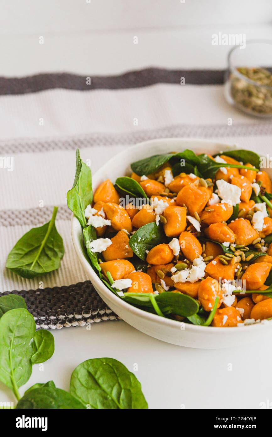 Kürbis-Gnocchi-Salat mit Feta-Käse und Baby-Spinatblättern mit weißem Hintergrund. Vegetarischer Salat, Mittagsrezept, einfaches Kochen Stockfoto