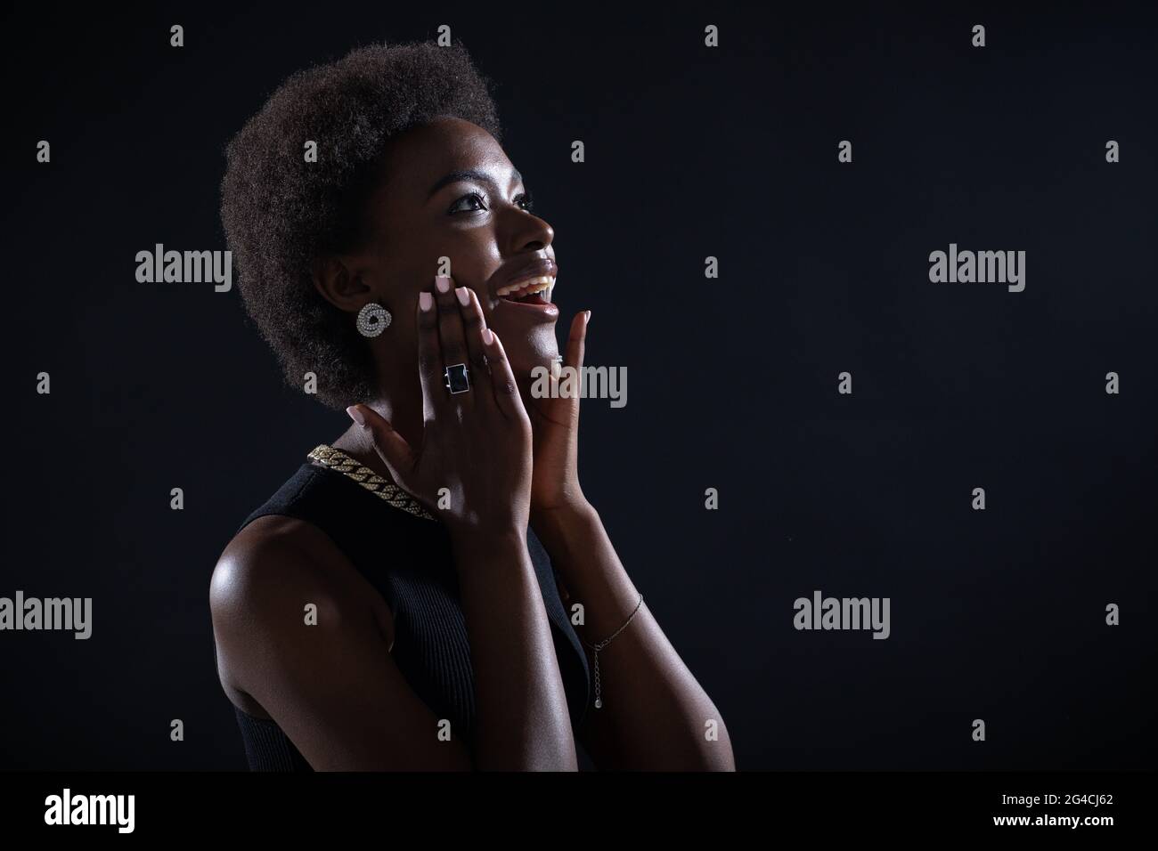 Beeindruckte junge afroamerikanische Frau mit erstaunlichem und glücklich bewundertem Ausdruck, isoliert auf schwarzem Hintergrund. Stockfoto