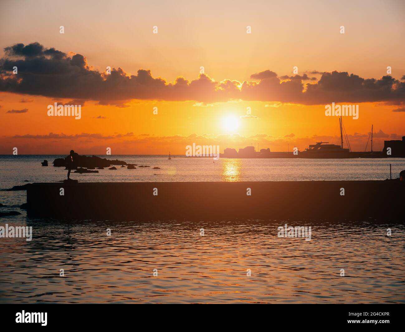 Tropisches Resort bei einem wunderschönen, farbenfrohen Sonnenuntergang über der Meeresoberfläche und der Silhouette eines Wellenbrechers. Stockfoto