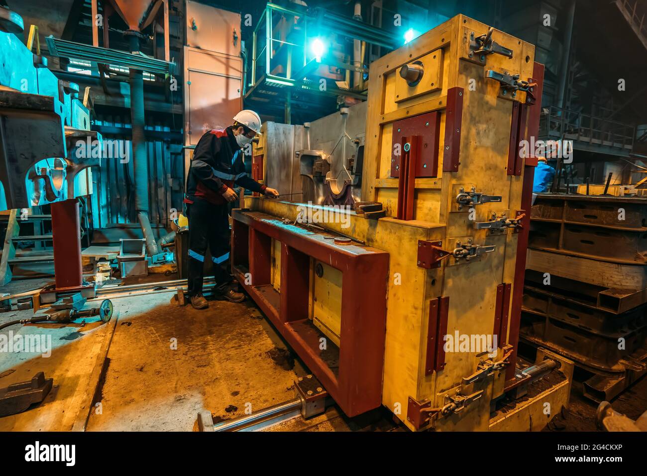 Der nicht erkennbare Arbeiter in der Uniform, der Helm und die schützende Gesichtsmaske arbeiten bei der Maschine in der Werkstatt der metallurgischen Anlage. Stockfoto