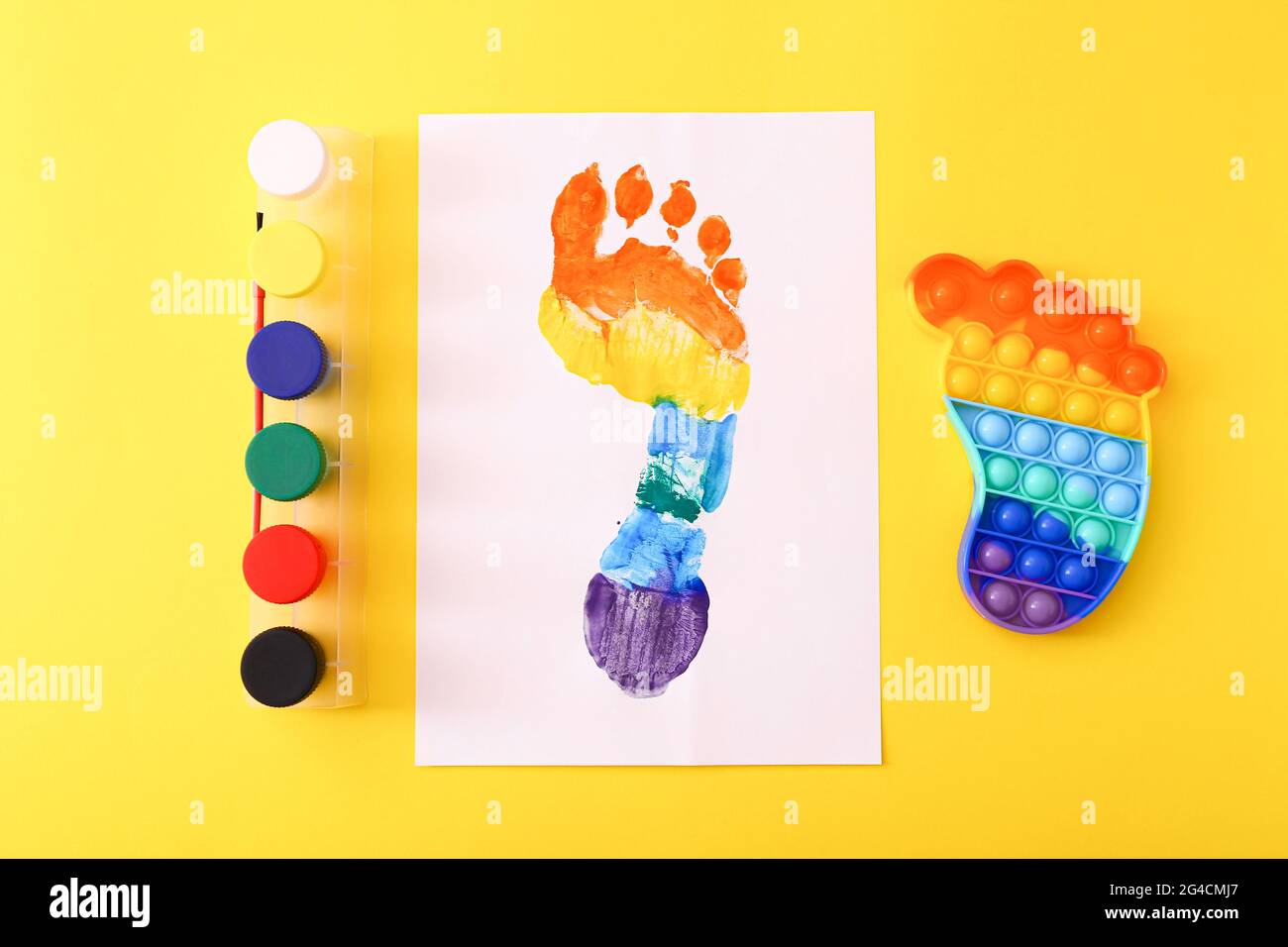 Neue trendige beliebte Silikon bunte Anti Stress Pop IT Spielzeug für Kinder und bunte Fußabdruck auf gelbem Hintergrund. Stockfoto