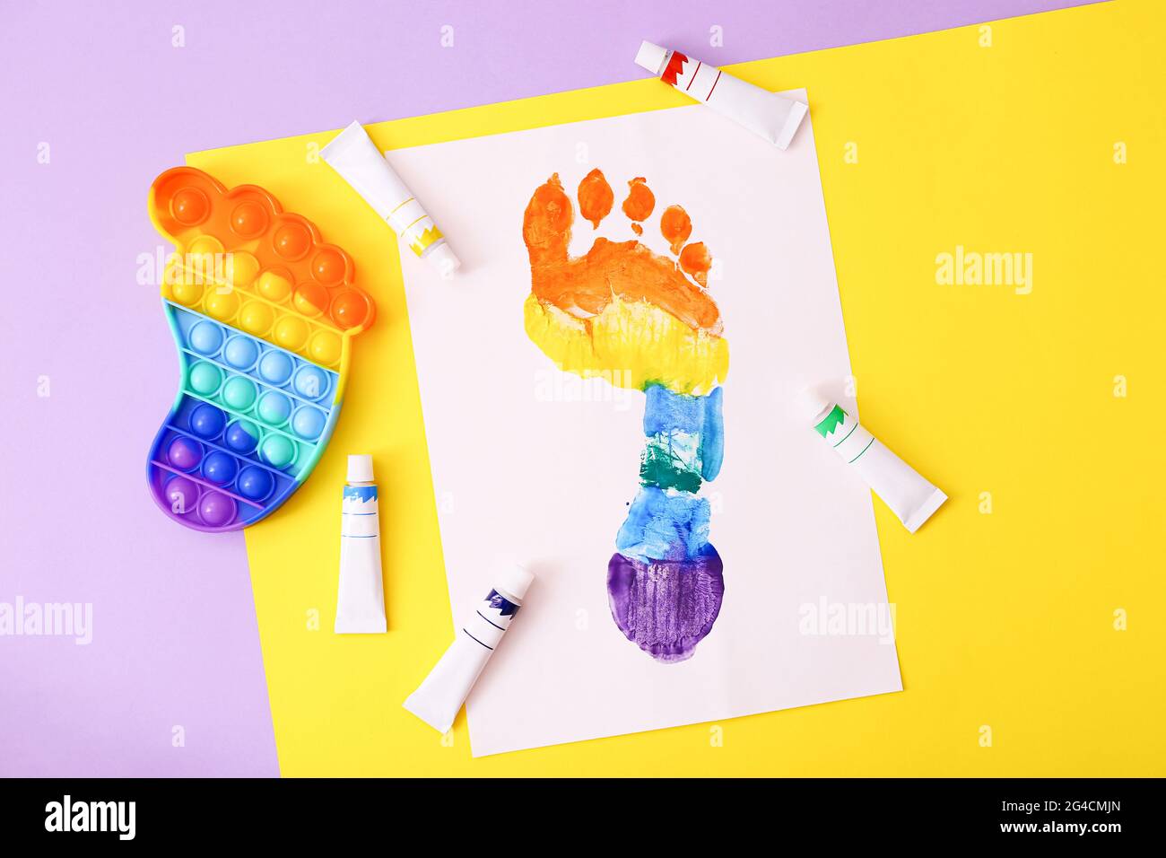 Neue trendige beliebte Silikon bunte Anti Stress Pop IT Spielzeug für Kinder und bunte Fußabdruck auf buntem Hintergrund. Stockfoto