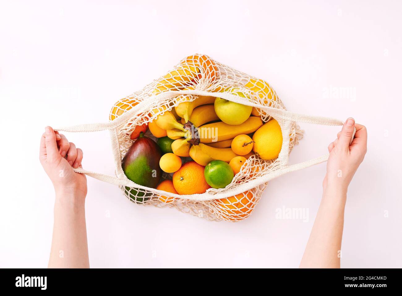 Weibliche Hand hält Mesh Eco-Tasche mit Früchten auf hellem Hintergrund. Gesunde, saubere Ernährung. Eco-Shopping-Konzept. Stockfoto