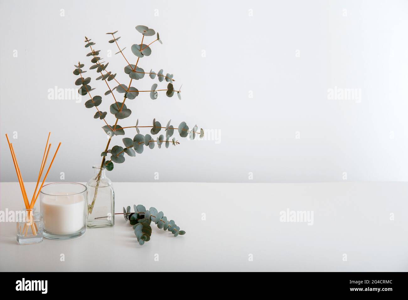 Aromatische Duftstäbchen, Duftkerze und Bukett aus Eukalyptuszweigen in Vase gegen weiße Wand auf dem Tisch. Komfort im Inneren des Hauses Stockfoto