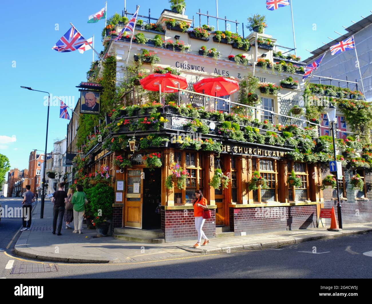 Das Äußere der Churchill Arms mit den Flaggen der Britischen Inseln, die fliegen. Der Pub ist berühmt für seine ganzjährigen Blumenarrangements. Stockfoto