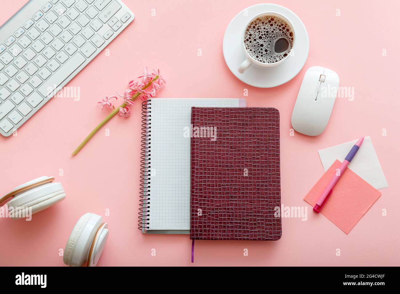 Girly Desktop mit Notizblöcke Computer Kopfhörer Tasse Kaffee auf rosa Hintergrund. Bürofläche. Schreibtisch für Schülerin oder Stockfoto