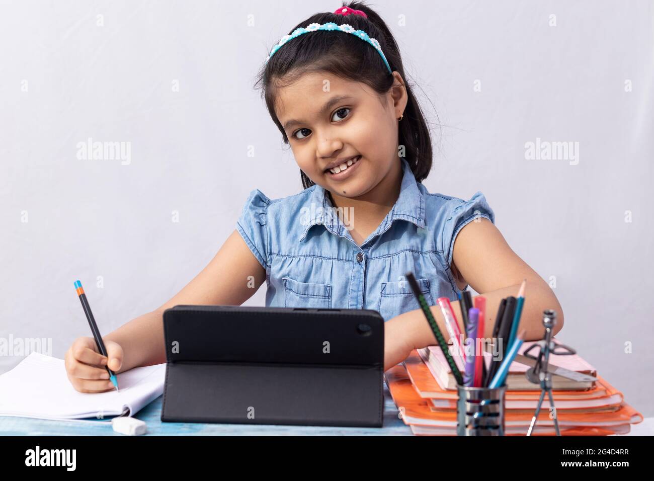 Ein hübsches indisches Mädchen, das während des Online-Kurses mit Tablet auf weißem Hintergrund die Kamera anschaut Stockfoto