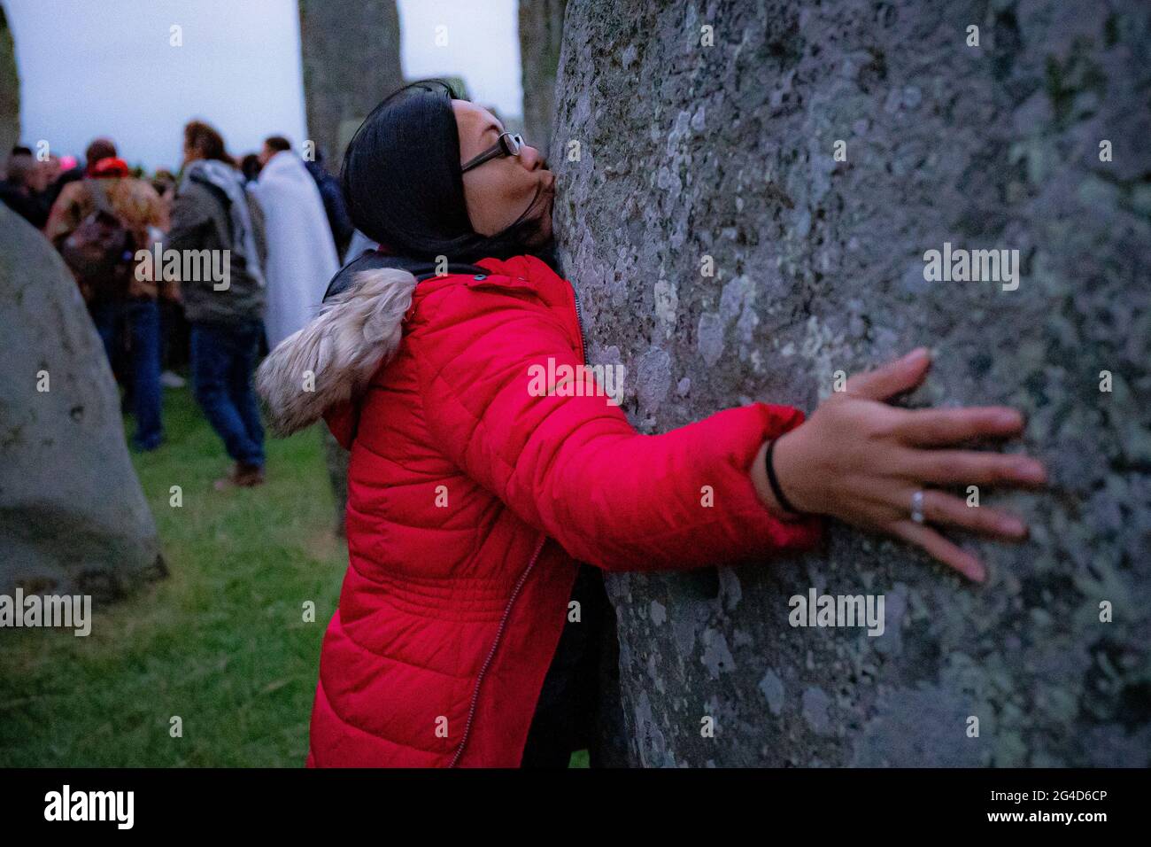 Eine Frau küsst einen Stein während der Sommersonnenwende in Stonehenge, wo einige Leute über den Zaun sprangen, um den Steinkreis zu betreten und den Sonnenaufgang am längsten Tag in Großbritannien zu beobachten. Die Steine wurden für die Feierlichkeiten, bei denen große Menschenmengen im Kreis zu sehen sind, aufgrund der Coronavirus-Lockdown-Erweiterung offiziell geschlossen. Bilddatum: Montag, 21. Juni 2021. Stockfoto