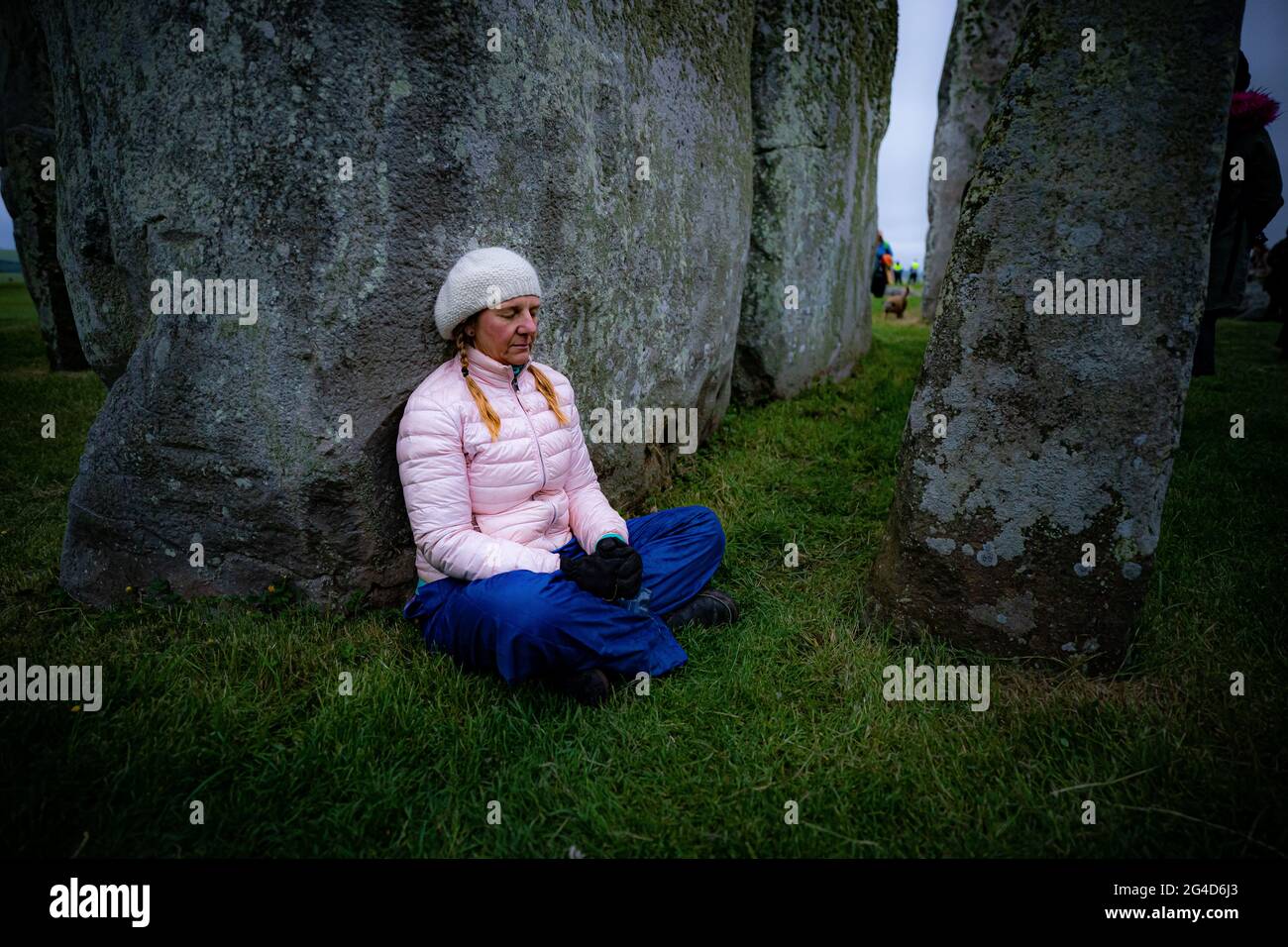 Während der Sommersonnenwende in Stonehenge sitzt eine Frau neben einem Stein, wo einige Leute über den Zaun sprangen, um den Platz zu betreten und den Sonnenaufgang am längsten Tag in Großbritannien zu beobachten. Die Steine wurden für die Feierlichkeiten, bei denen große Menschenmengen im Kreis zu sehen sind, aufgrund der Coronavirus-Lockdown-Erweiterung offiziell geschlossen. Bilddatum: Montag, 21. Juni 2021. Stockfoto