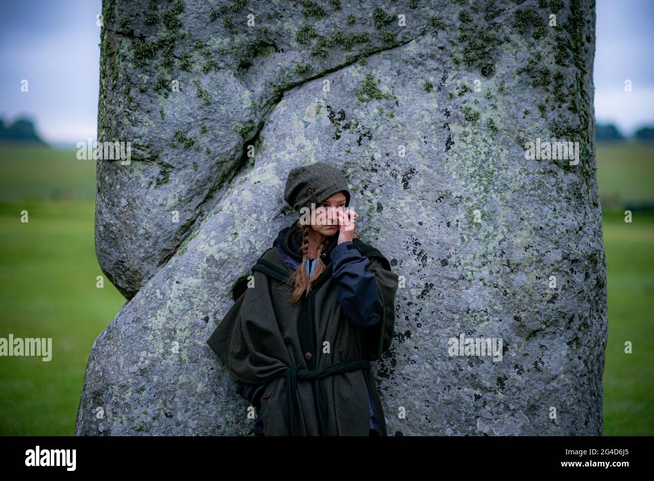 Während der Sommersonnenwende in Stonehenge steht eine Frau neben einem Stein, wo einige Leute über den Zaun sprangen, um den Platz zu betreten und den Sonnenaufgang am längsten Tag in Großbritannien zu beobachten. Die Steine wurden für die Feierlichkeiten, bei denen große Menschenmengen im Kreis zu sehen sind, aufgrund der Coronavirus-Lockdown-Erweiterung offiziell geschlossen. Bilddatum: Montag, 21. Juni 2021. Stockfoto