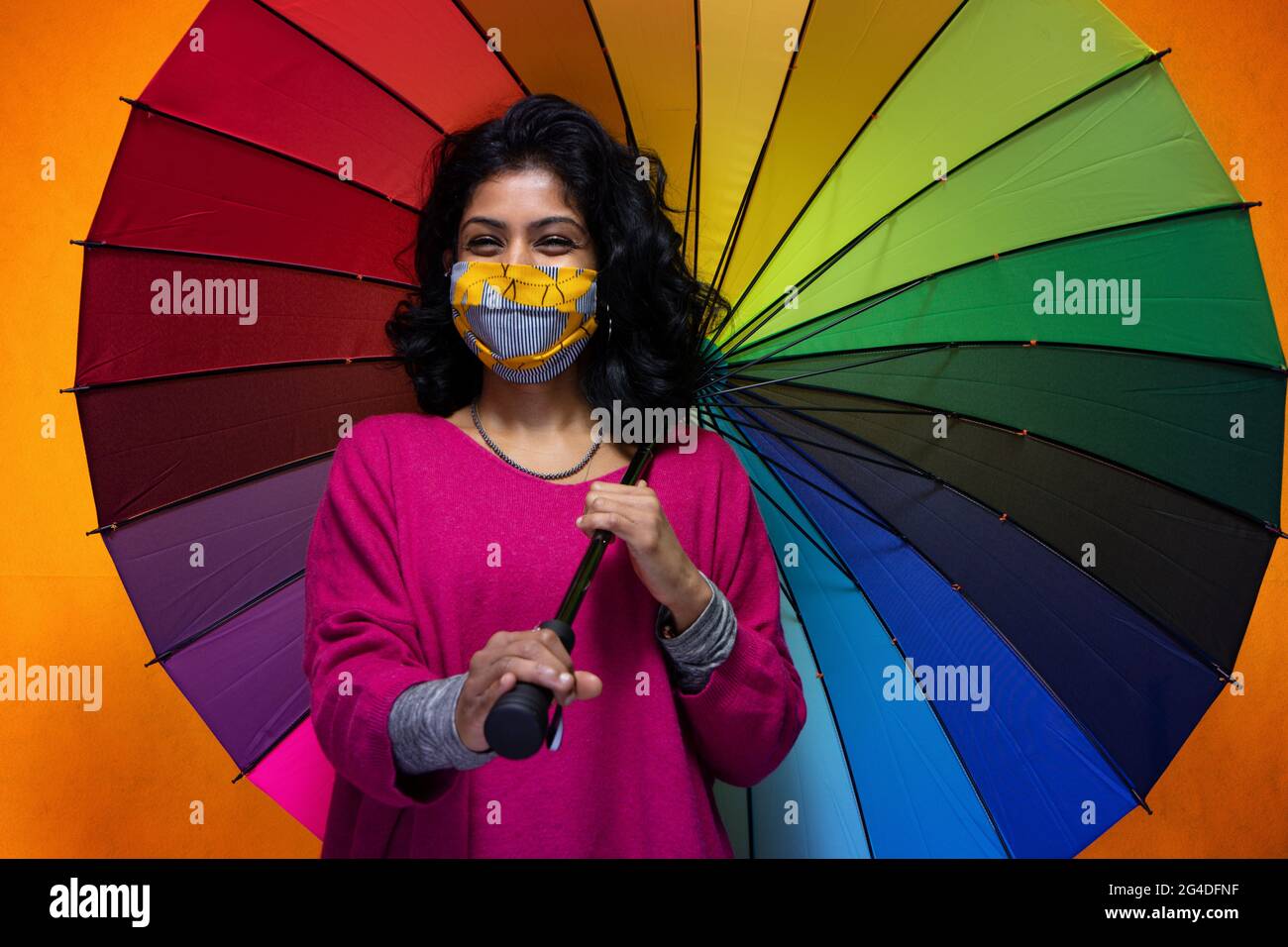 Schöne junge indische Frau posiert mit einem farbigen Regenschirm mit Covid 19 Maske Schutz - hübsche Sri Lanka Mädchen verwendet Schutz vor pandemischen Rauchgasklassen Stockfoto