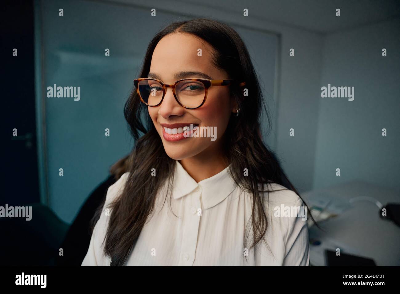 Porträt einer lächelnden jungen Geschäftsfrau mit Brillen, die im Büro der Firma auf die Kamera schaut Stockfoto