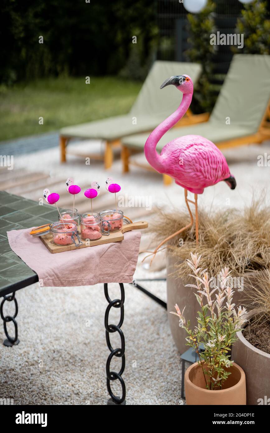 Eis in Gläsern mit rosa Flamingoflaggen und Skulpturen auf einer Terrasse im Freien. Konzept eines Sommersnacks Stockfoto