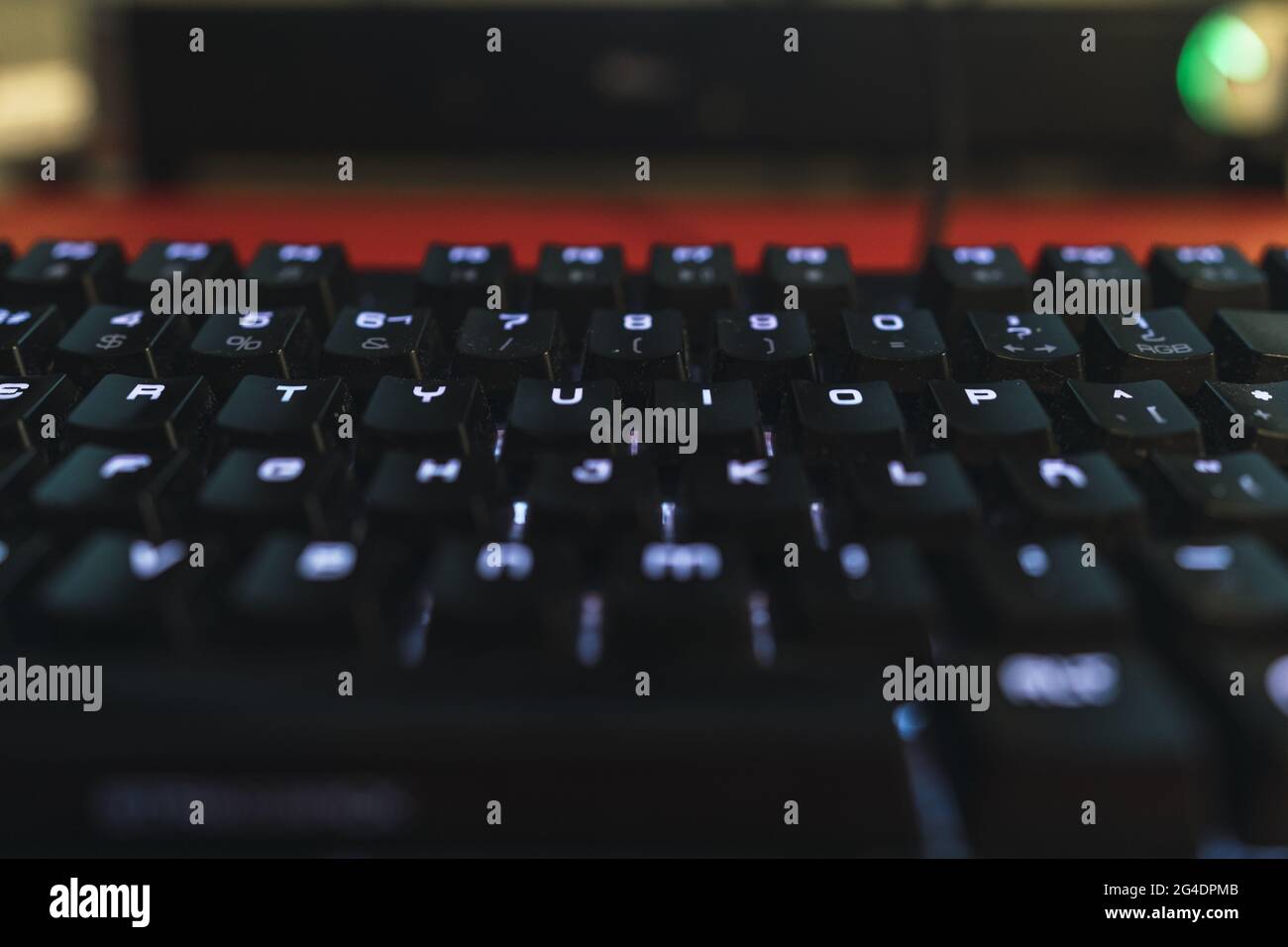Nahaufnahme des mittleren Teils einer schwarzen Tastatur mit weißen rgb-Lichtern auf rotem Tisch Stockfoto