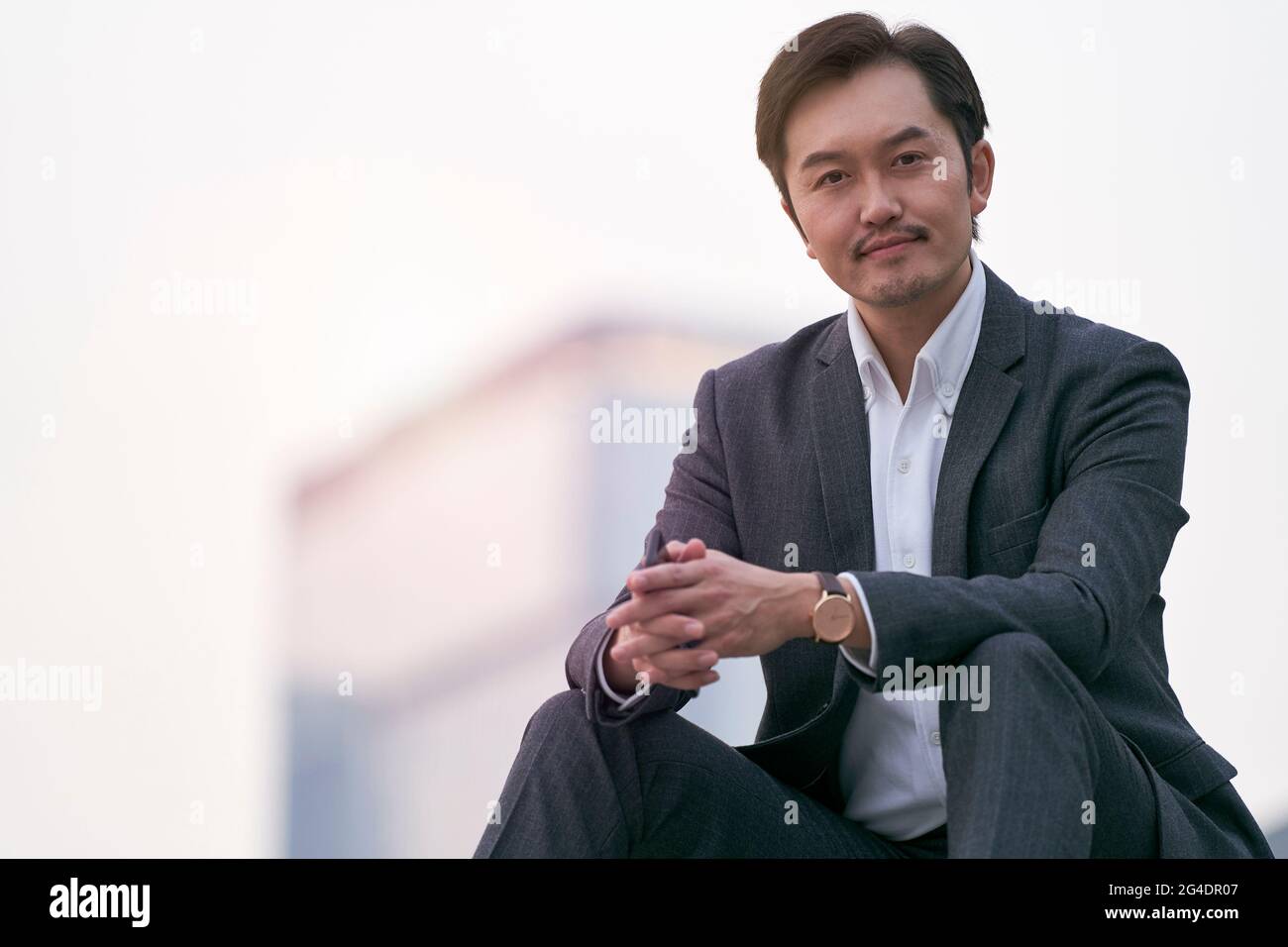 Außenportrait eines erfolgreichen asiatischen Geschäftsmanns, der in Vollanzug auf einer Treppe sitzt Stockfoto