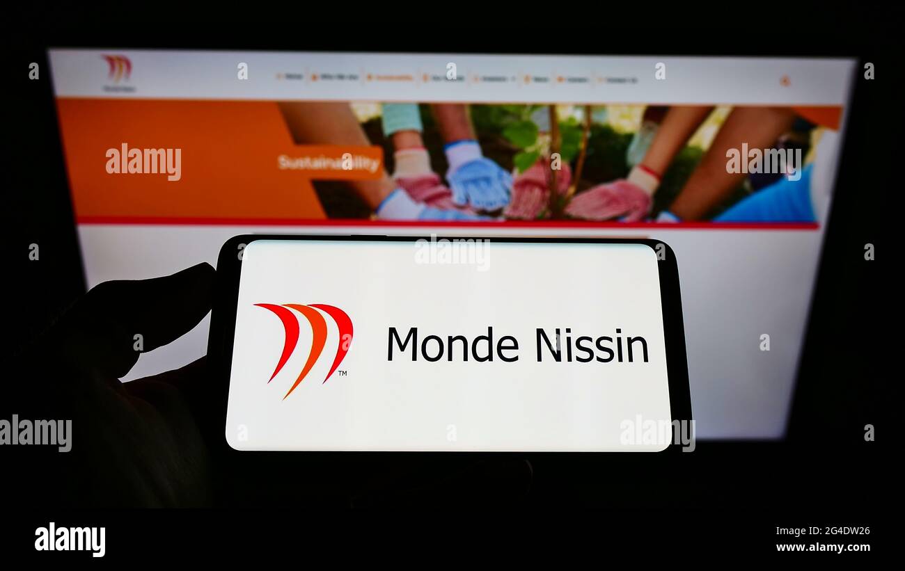 Person mit Mobiltelefon und Logo des philippinischen Lebensmittelunternehmens Monde Nissin Corporation auf dem Bildschirm vor der Webseite. Konzentrieren Sie sich auf die Telefonanzeige. Stockfoto