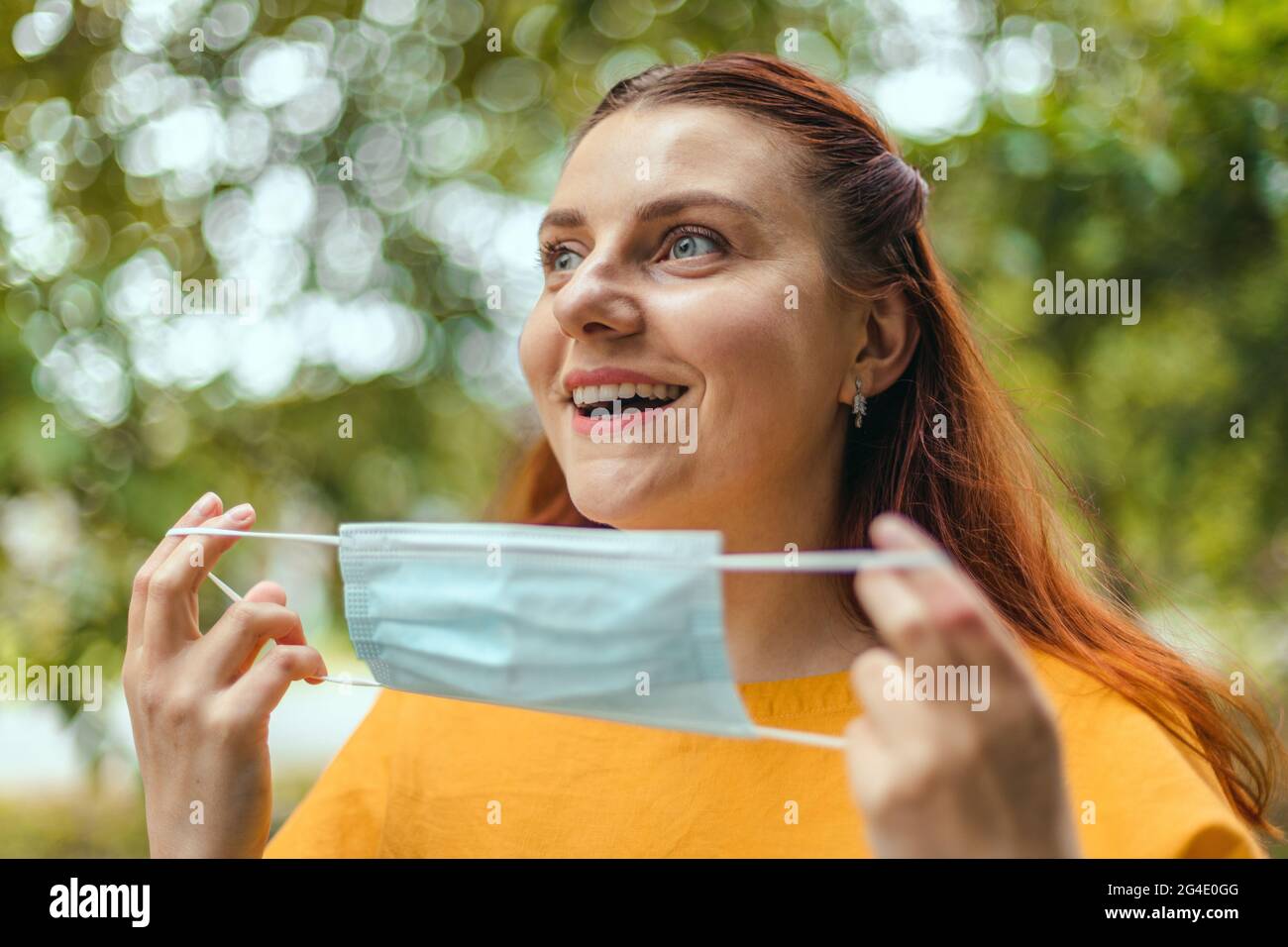 Glückliche Frau zieht ihre schützende medizinische Maske aus ihrem Gesicht  und genießt die Natur und die frische Luft nach dem Ende der  Coronavirus-Pandemie Stockfotografie - Alamy