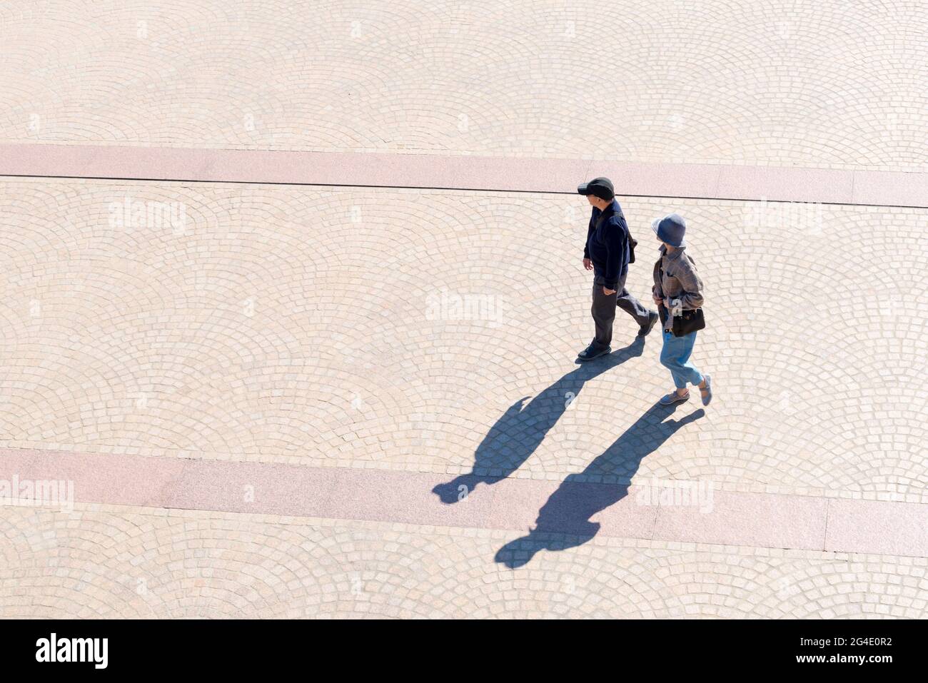 Ein älteres asiatisches Paar wirft lange Schatten, als sie an einem sonnigen Morgen in New South Wales, Australien, über den Vorplatz des Opernhauses von Sydney laufen Stockfoto