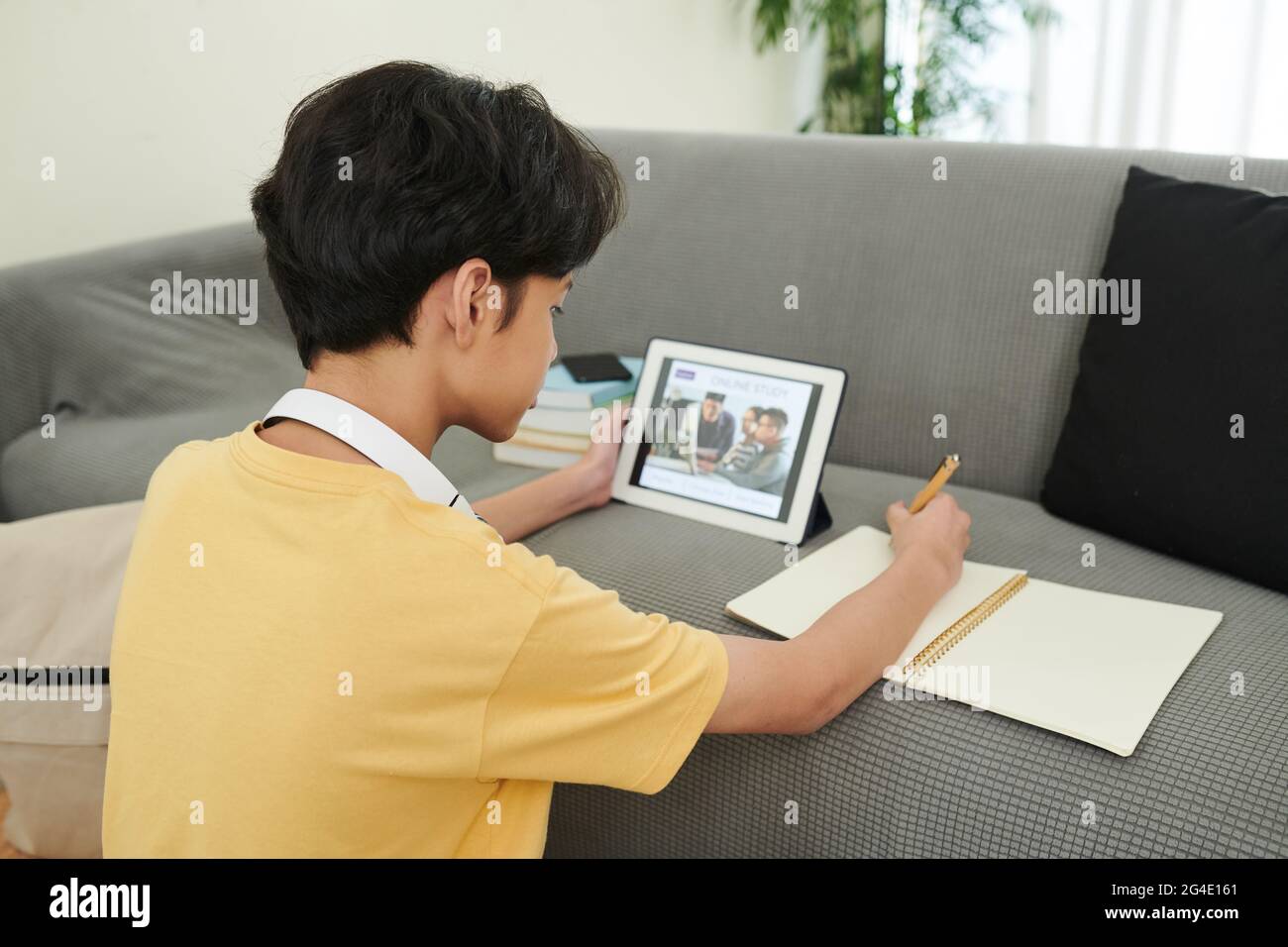 Teenager, der Online-Kurs besucht, sich am Tablet-Computer eine Lektion ansieht und in Lehrbüchern schreibt Stockfoto