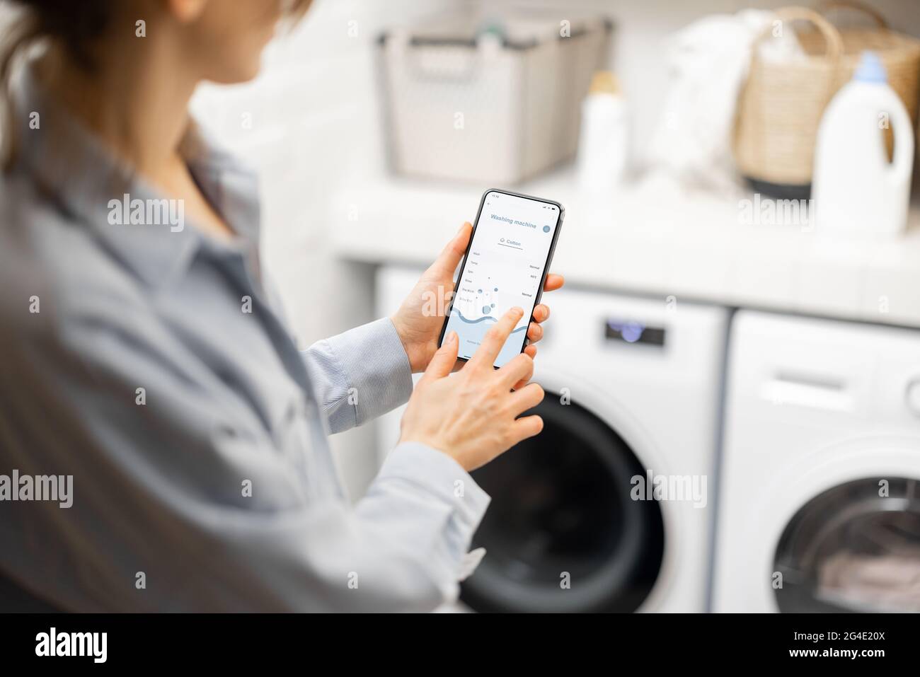 Die Frau steuert die Waschmaschine mit einem Smartphone Stockfoto