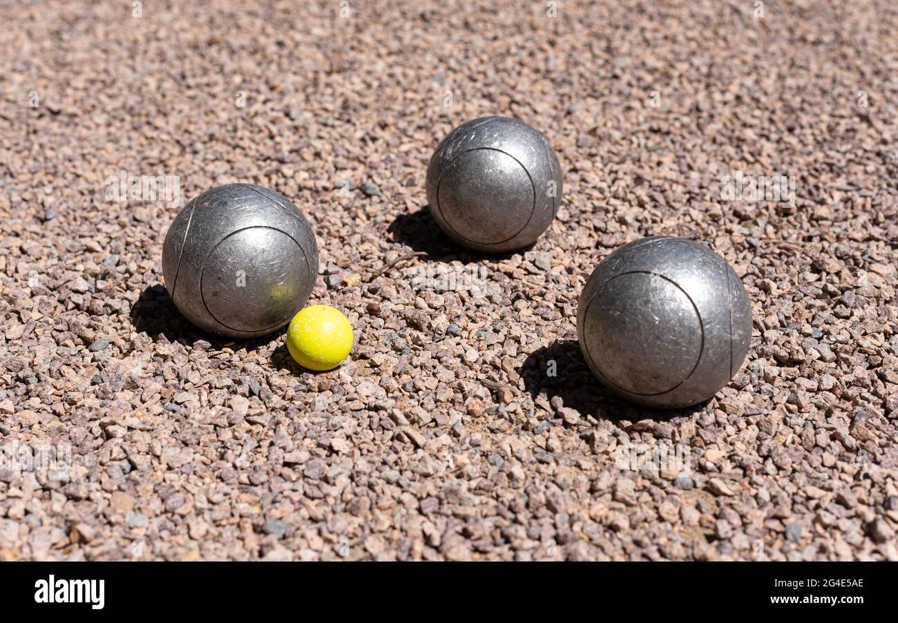 Drei Petanque-Kugeln (Boule) in der Nähe eines gelben Buben zielen auf einen rosa Kiesboden. Stockfoto