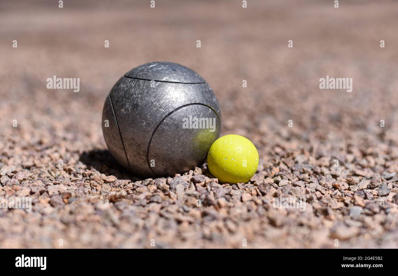 Eine Boule (Petanque Ball) in der Nähe eines gelben Buben Zielballs auf einem rosa Kiesboden. Stockfoto