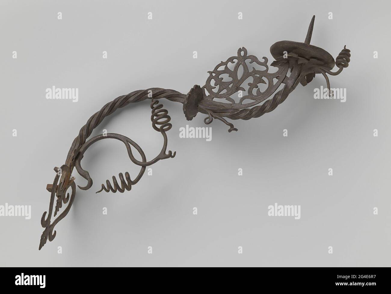 Leichter Arm aus geschmiedetem Eisen, verdreht und S-förmig gebogen. Ein geschmiedeter, leichter Eisenarm, gebogen und in S-Form; zur Hälfte mit einem gezahnten Knoten, über dem ein üppiges Blattornament und ein spaltender Ast, der in zwei Spiralen endet, zu sehen ist. Stockfoto