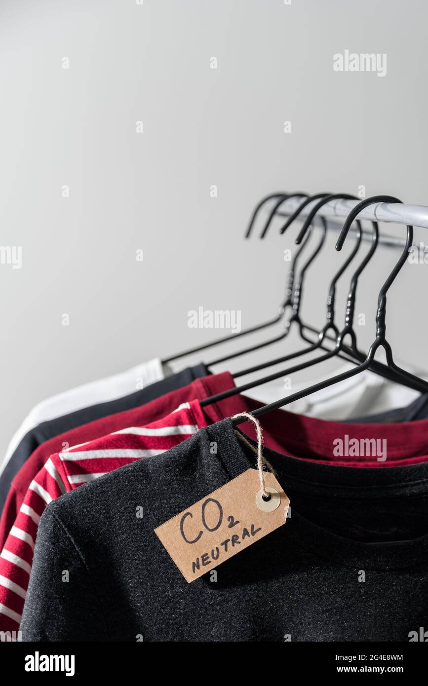 Kleidung auf Kleiderbügeln in der Schiene mit Recycling-Etikett aus CO2-Emissionspapier Stockfoto
