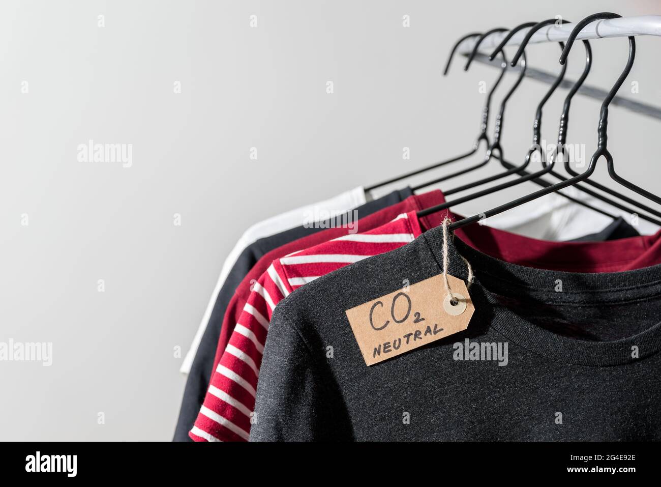 Kleidung auf Kleiderbügeln in der Schiene mit Recycling-Etikett aus CO2-Emissionspapier Stockfoto