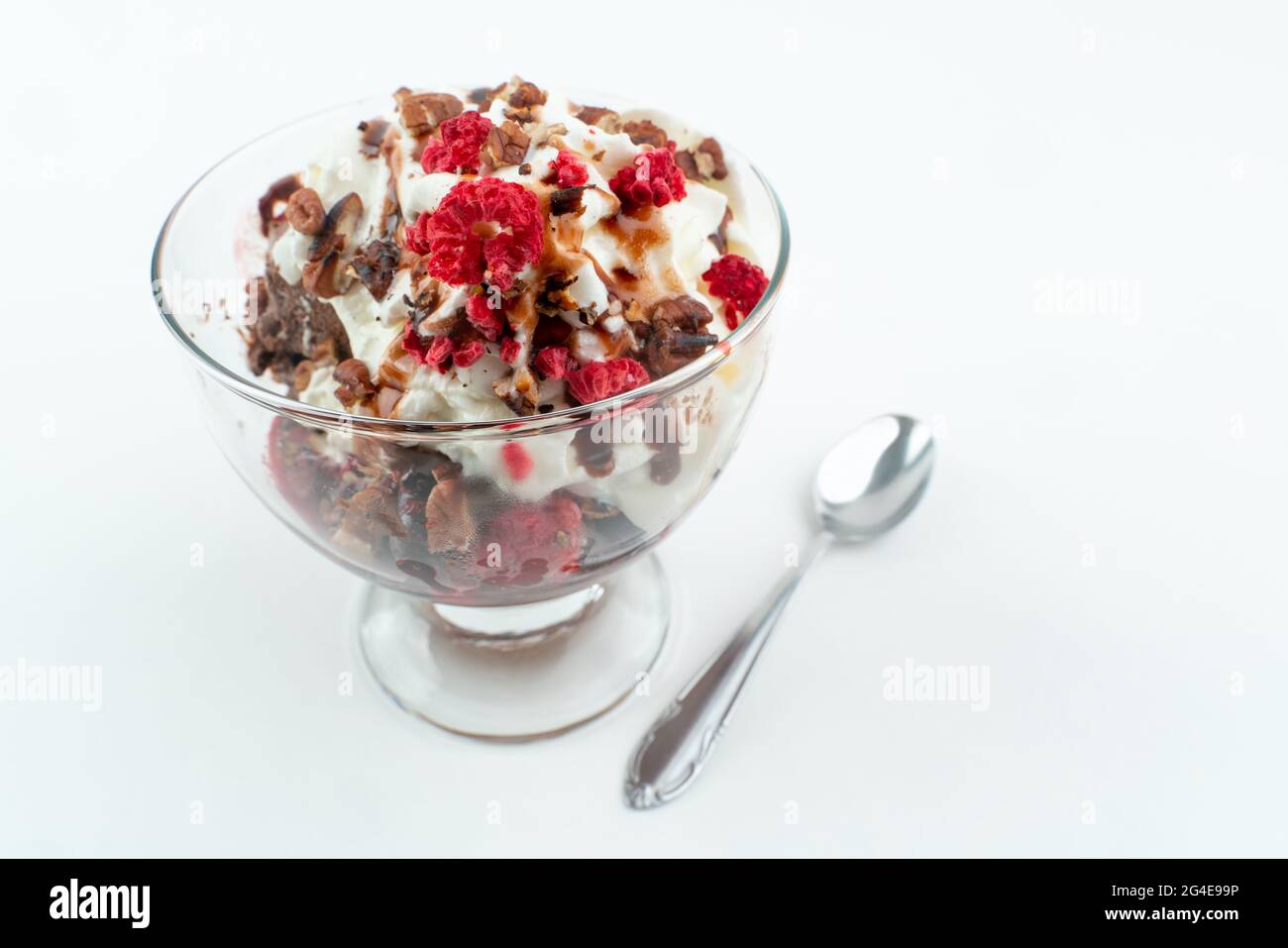 Schokoladeneis mit einer Creme, verschiedenen Nüssen und gefrorenen Beeren auf der Oberseite, in einer Glastasse, isoliert auf weißem Hintergrund Stockfoto