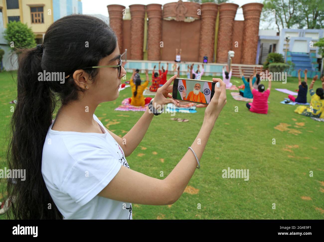 Beawar, Indien. Juni 2021. Ein Mädchen beobachtet die Ansprache des indischen Premierministers Narendra Modi auf ihrem Mobiltelefon, während eine Gruppe von Frauen beim siebten Internationalen Yoga-Tag in Beawar Yoga durchführt. PM Modi startet die mYoga-App, die weltweit verfügbar sein wird. Dies wird dazu beitragen, das Motto ‘eine Welt, eine Gesundheit“ zu erfüllen. (Foto: Sumit Saleswat/Pacific Press) Quelle: Pacific Press Media Production Corp./Alamy Live News Stockfoto