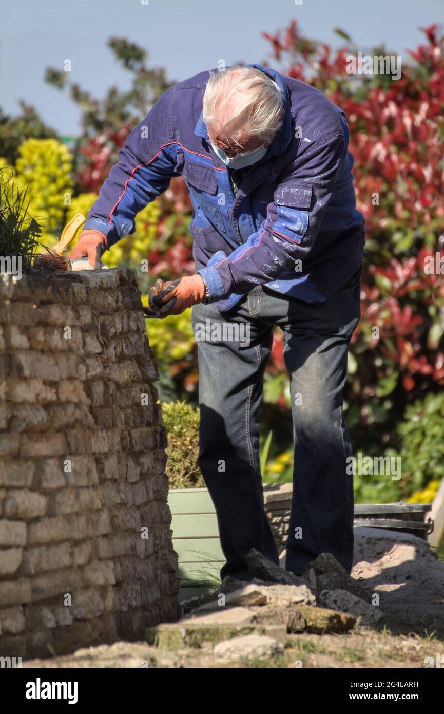 Älterer Mann, Baumeister Zementieren, Zeigen EINER rustikalen Steinwand mit EINEM Tuck Pointer Tool England Großbritannien Stockfoto