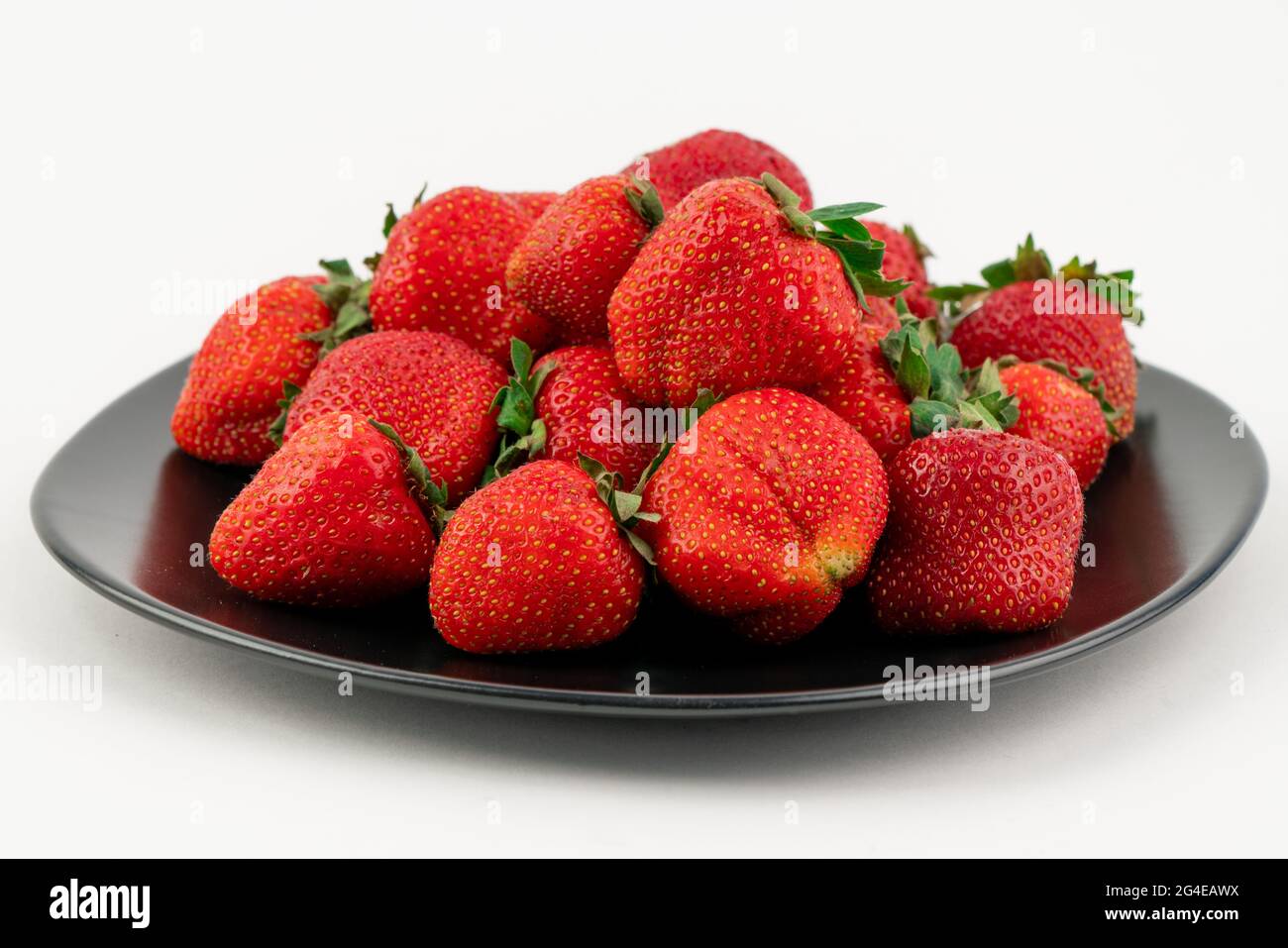 Viele rote reife Erdbeeren auf einem schwarzen Teller isoliert auf weißem Hintergrund Stockfoto