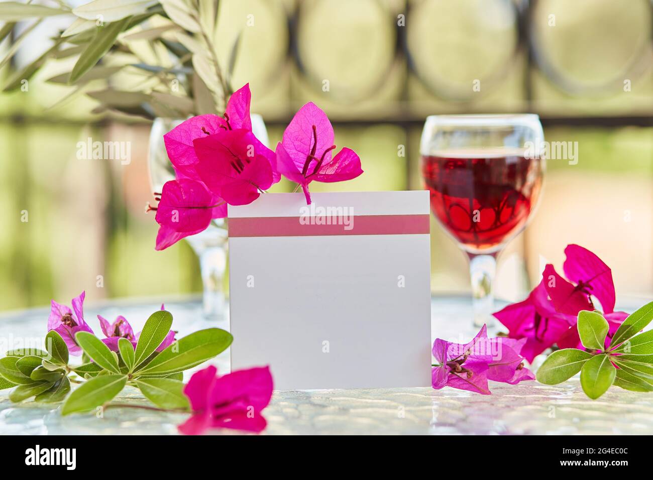 Nachbau einer Postkarte, Einladung. Elegantes Glas Rotwein. Dekorative rosa Blüten von Bougainvillea. Festliches, kreatives Urlaubskonzept. Dekorativer gre Stockfoto