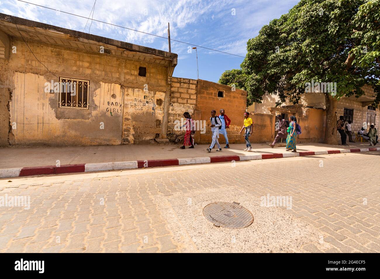 MBOUR, SENEGAL - JANUAR CIRCA, 2021. Unbekannte Mädchen und Jungen im schulpflichtigen Alter mit Rucksack, die im sonnigen Frühling nach der Schule in dem armen Dorf spazieren gehen Stockfoto