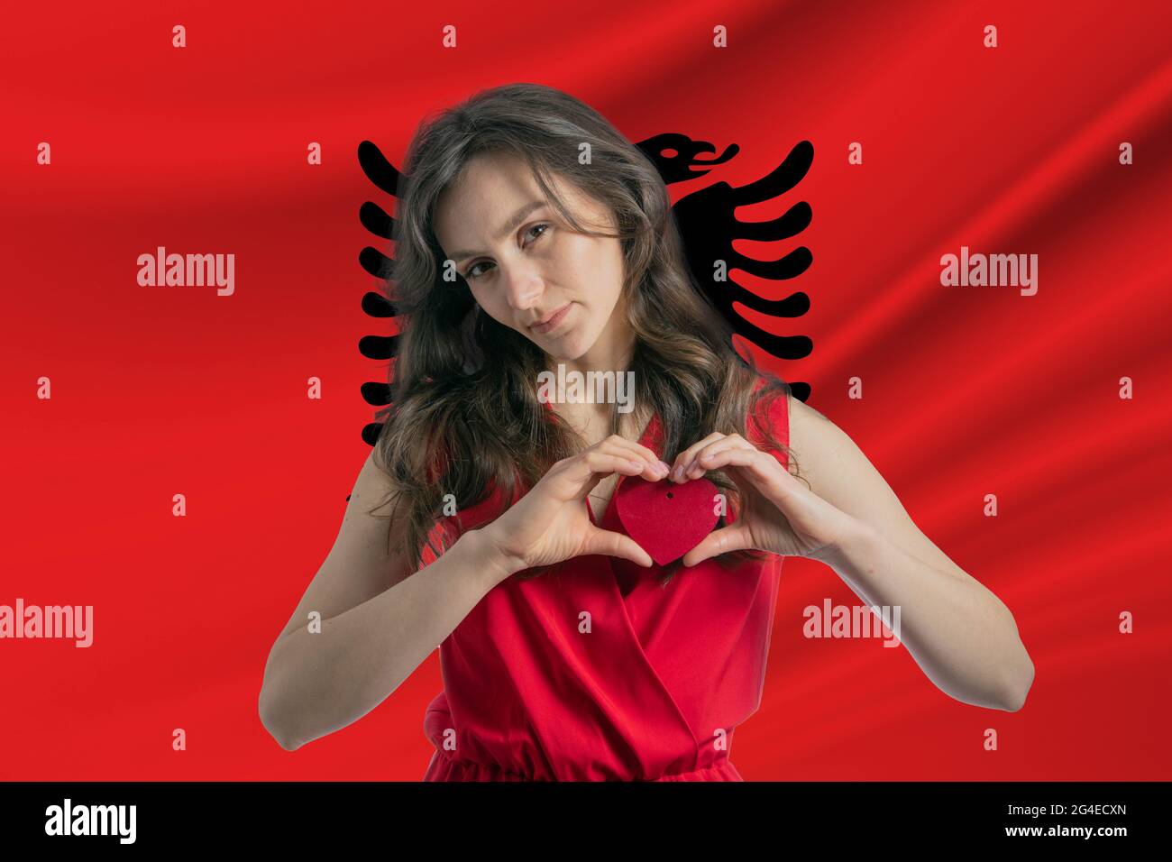 Ich Liebe Albanien. Ein Mädchen hält vor dem Hintergrund der Flagge Albaniens ein Herz auf ihrer Brust in den Händen. Der Begriff des Patriotismus. Stockfoto