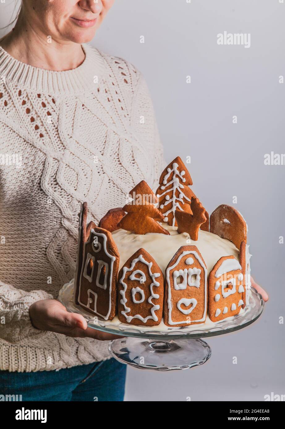 Frau hält hausgemachten Kuchen mit Lebkuchen Stadthaus Fassaden, einen Weihnachtsbaum und Rentiere auf Glasständer Stockfoto