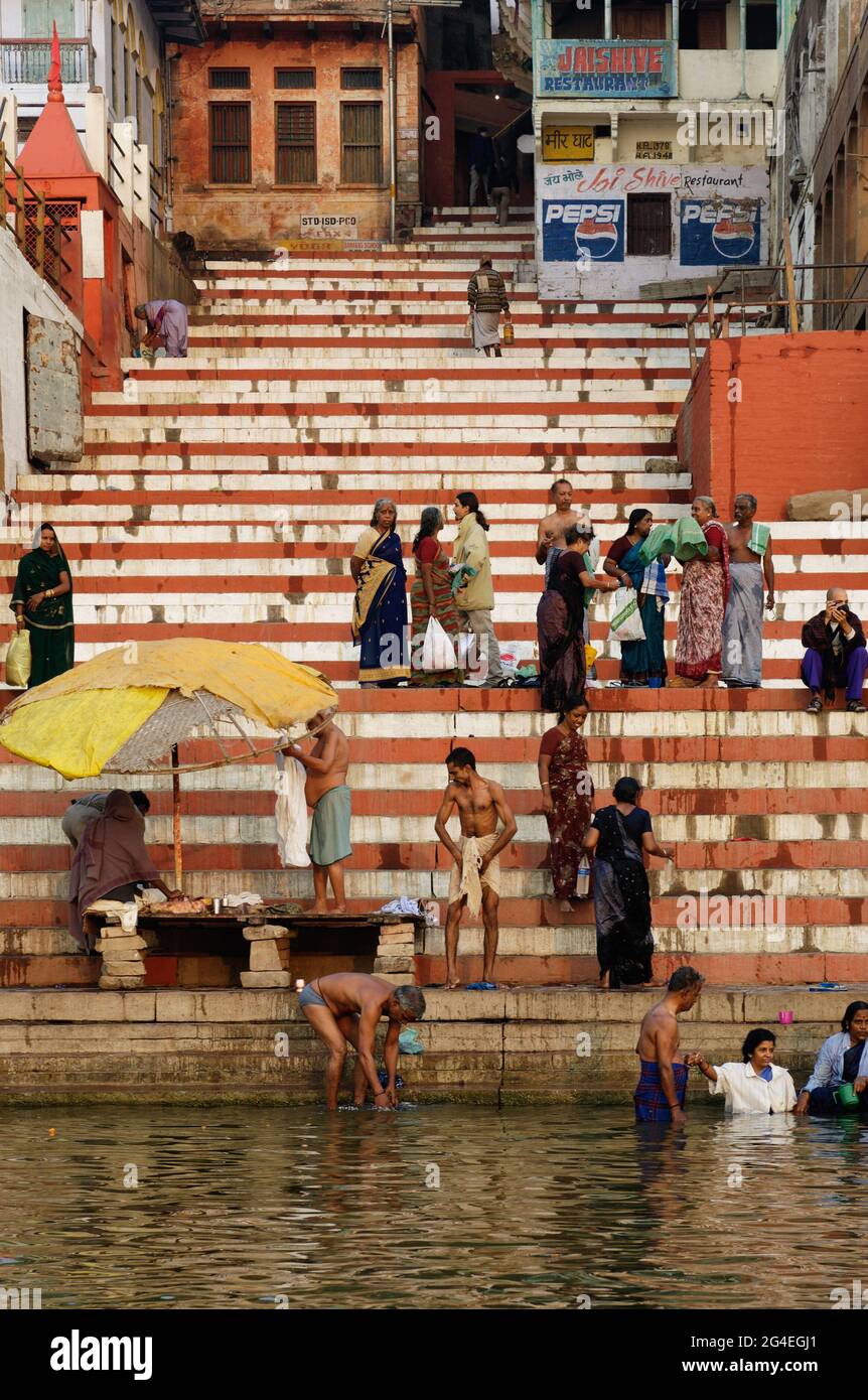 Morgenbadende nach ritueller Reinigung am Ufer des Ganges durch rot-weiß gestreifte Stufen des Meer Ghat in Varanasi, Indien Stockfoto