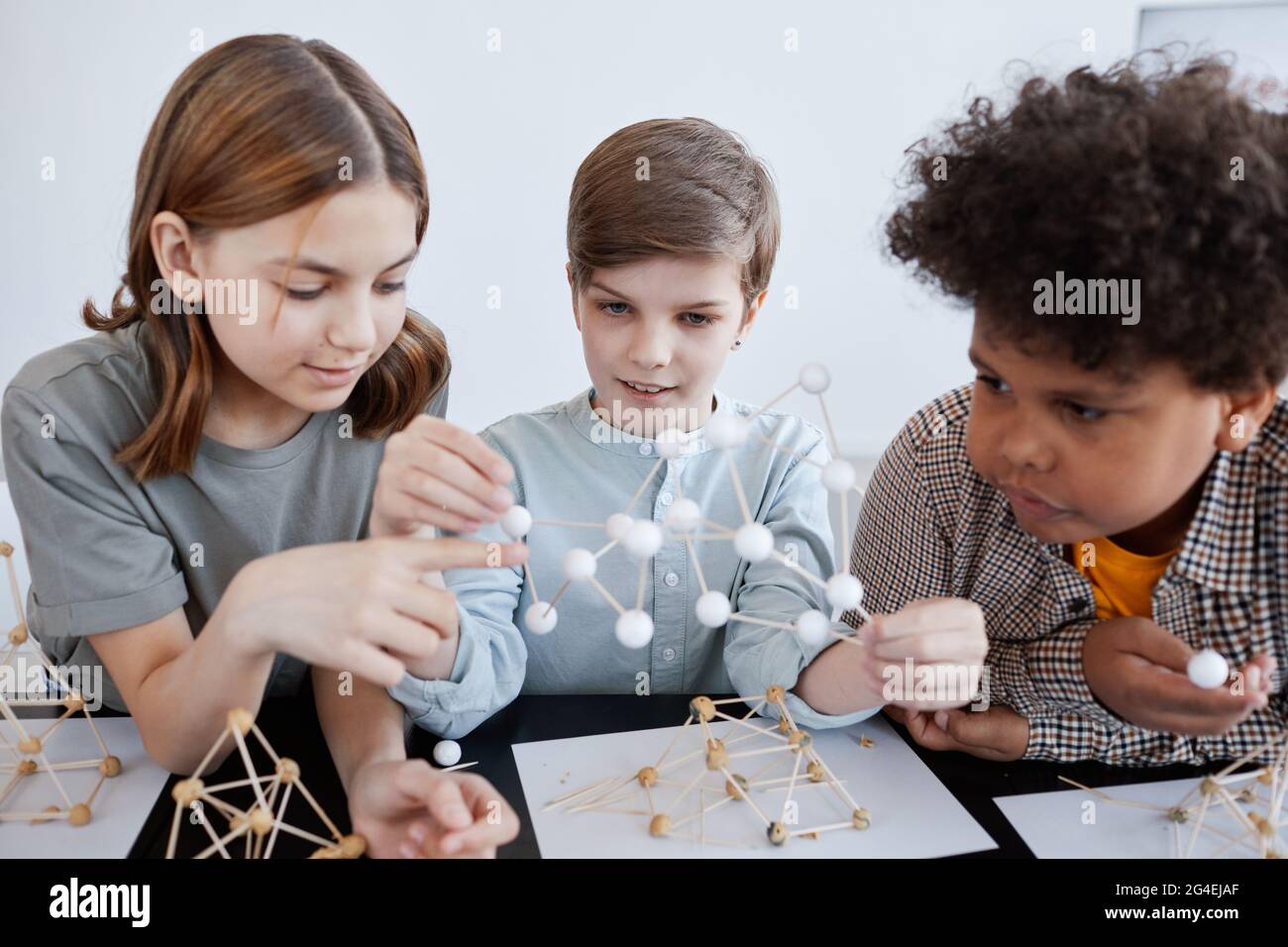Gruppe von drei Kindern, die während des Kunst- und Handwerkskurzens in der Schule mit Holzmodellen spielen Stockfoto