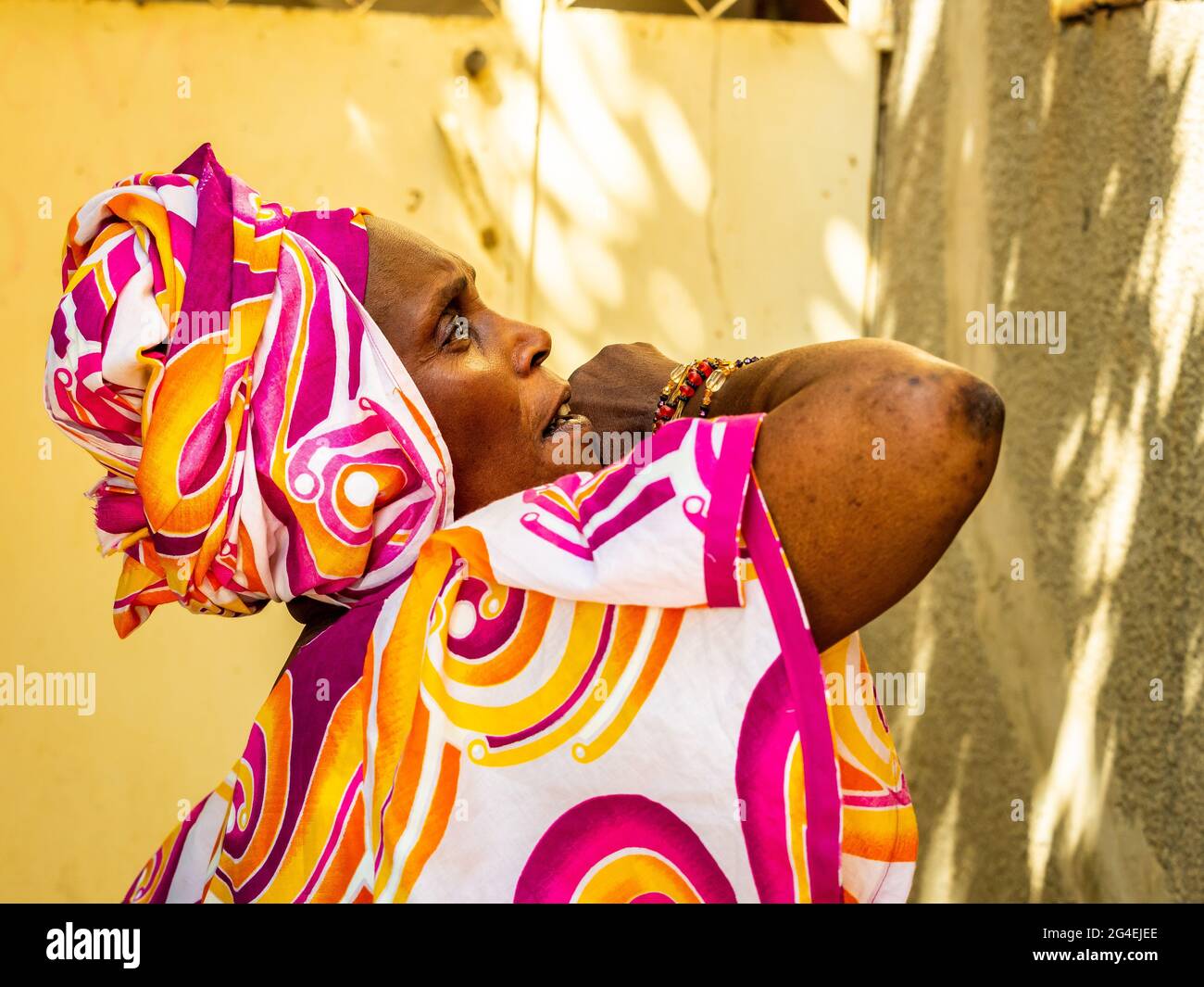 MBOUR, SENEGAL - JANUAR CIRCA, 2021. Nicht identifizierte senegalesische ziemlich reife Frau in traditionellem Kleid im Freien, die lächelnd aufschaut. Armut und Glück Stockfoto