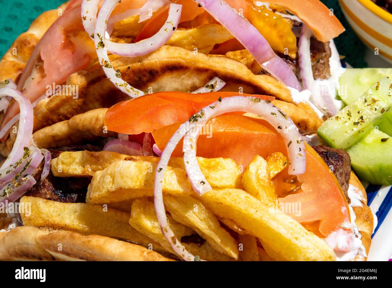 Nahaufnahme einer leckeren Burger-Pita mit Tsatziki-Sauce, frischen Naxian-Kartoffeln, Pommes Frites und Gurkensalat. Stockfoto