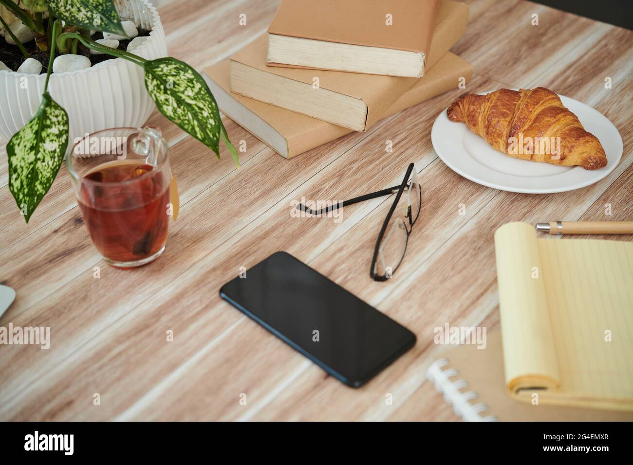 Stapel von Büchern, Smartphone, Tee und Croissant auf dem Tisch des Studenten Stockfoto