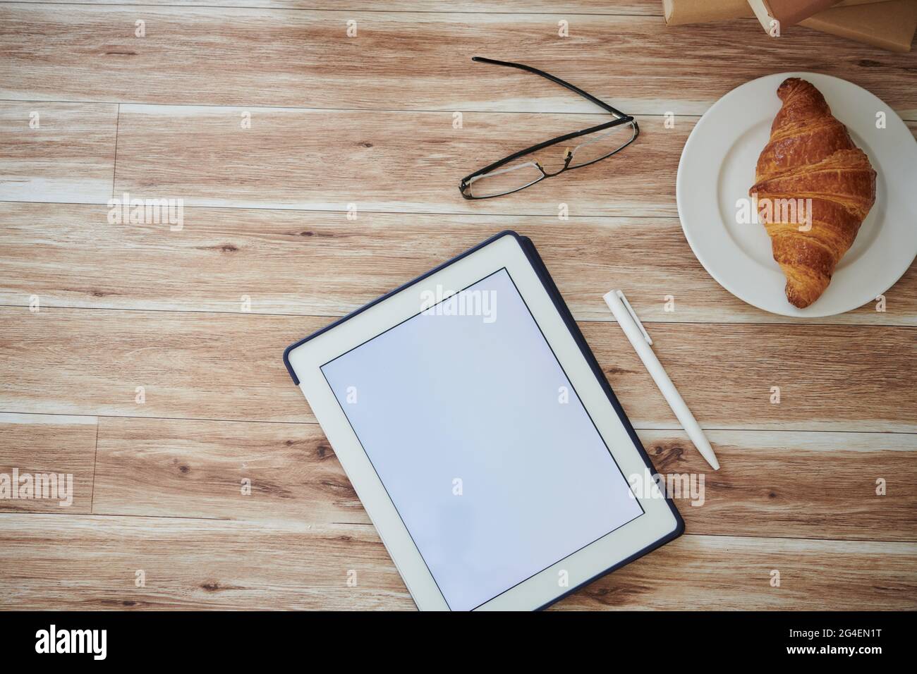 Digitales Tablet mit leerem Bildschirm, Gläsern und Teller mit frischem, köstlichem Croissant, Blick von oben Stockfoto