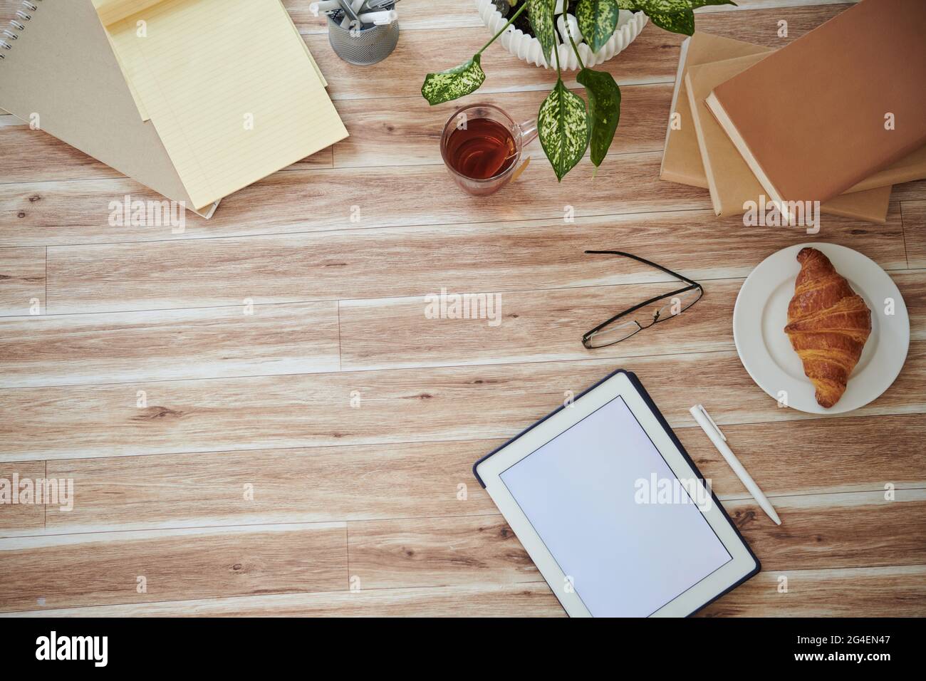 Tablet-Computer mit leerem Bildschirm, Büchern, Croissants und Gläsern auf dem Tisch, Blick von oben Stockfoto
