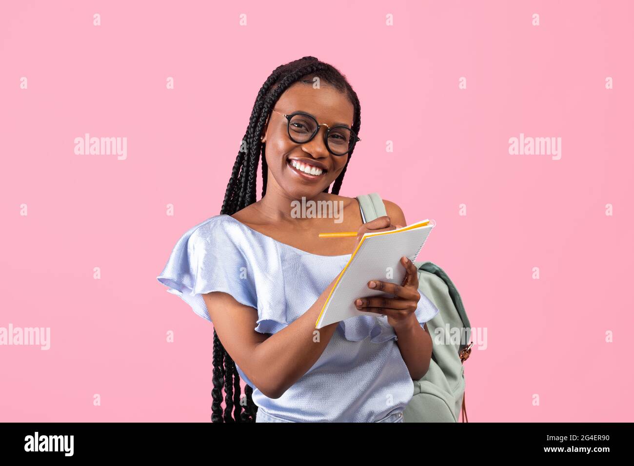 Smart junge schwarze Frau mit Rucksack tragen Brille, Notizen über rosa Studio-Hintergrund. Hochschulbildung Stockfoto