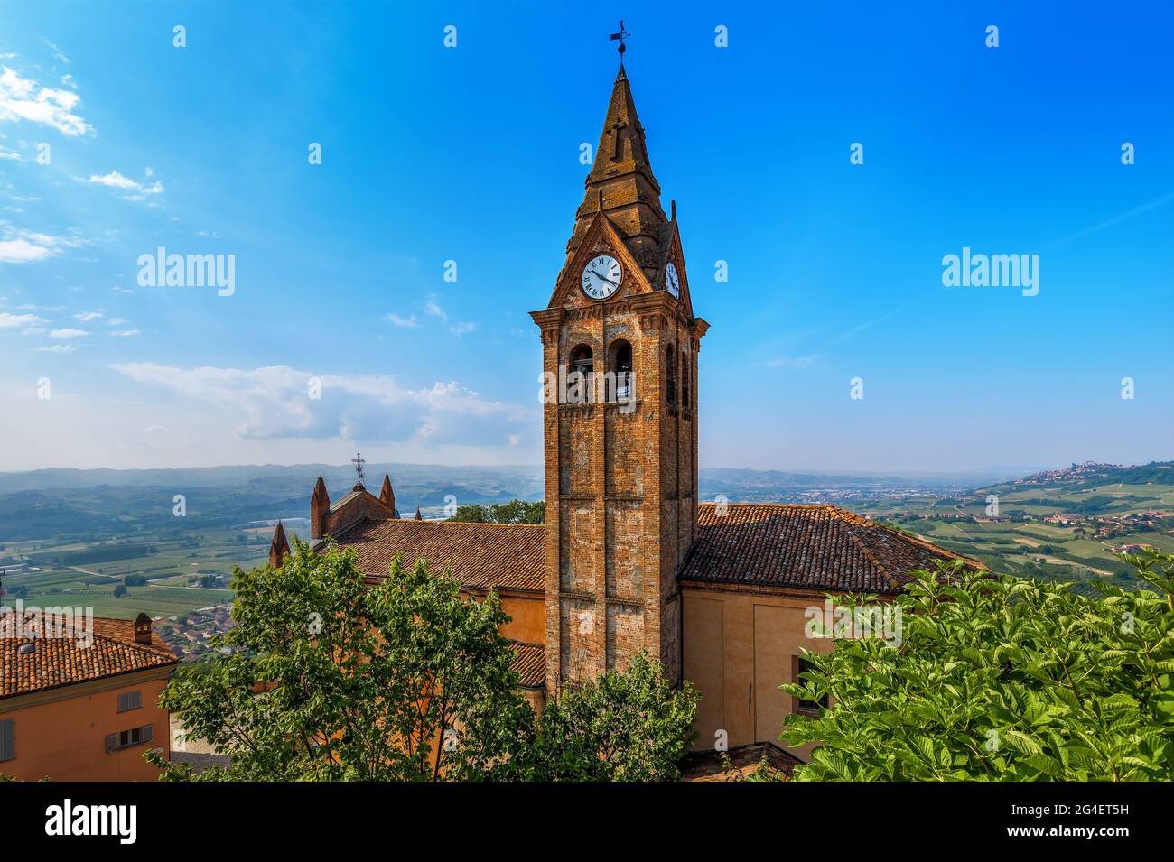 Blick von oben auf das Kirchendach und den alten Ziegelglockenglockener mit Uhr unter blauem Himmel in der Kleinstadt Magliano Alfieri im Piemont, Norditalien. Stockfoto