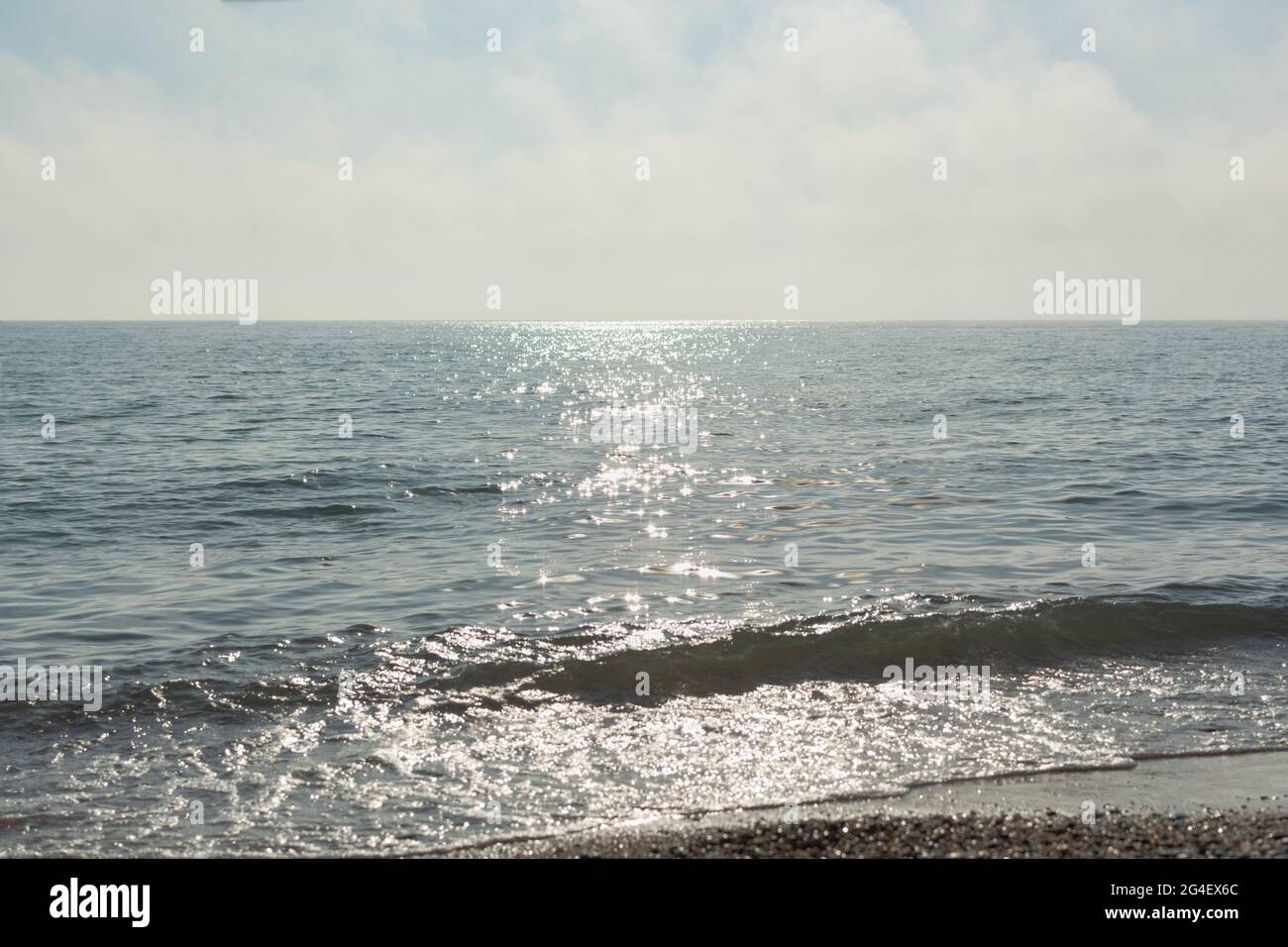 Silbernes Meer glitzernden Hintergrund. Minimalistische Sommerlandschaft in Grau- und Silbertönen. Mittags heißer Tag. Die helle Sonne spiegelt sich in den Wellen wider Stockfoto