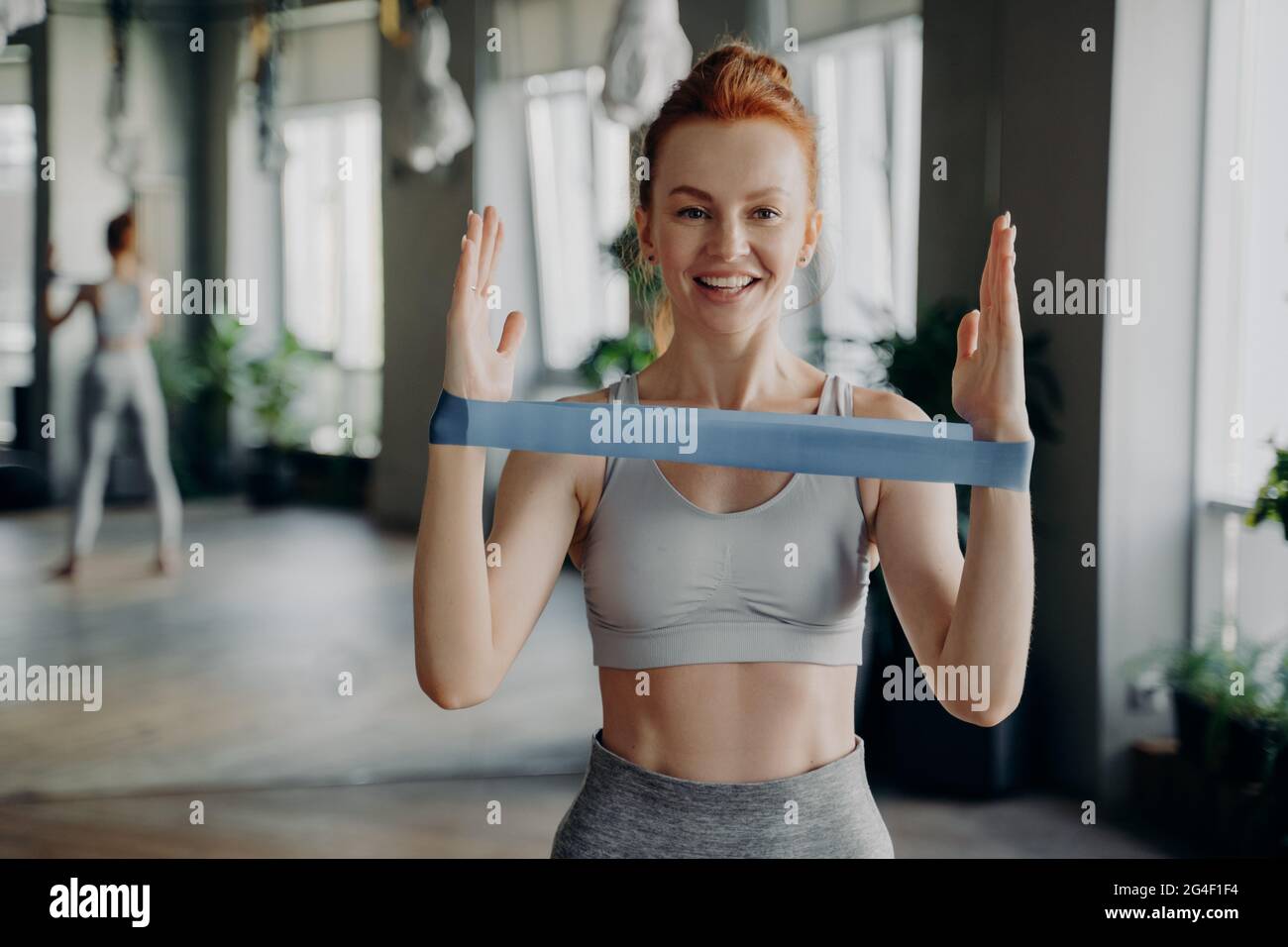 Porträt einer jungen sportlichen Rothaarigen Frau in Sportbekleidung mit Widerstand Gummiband Stockfoto